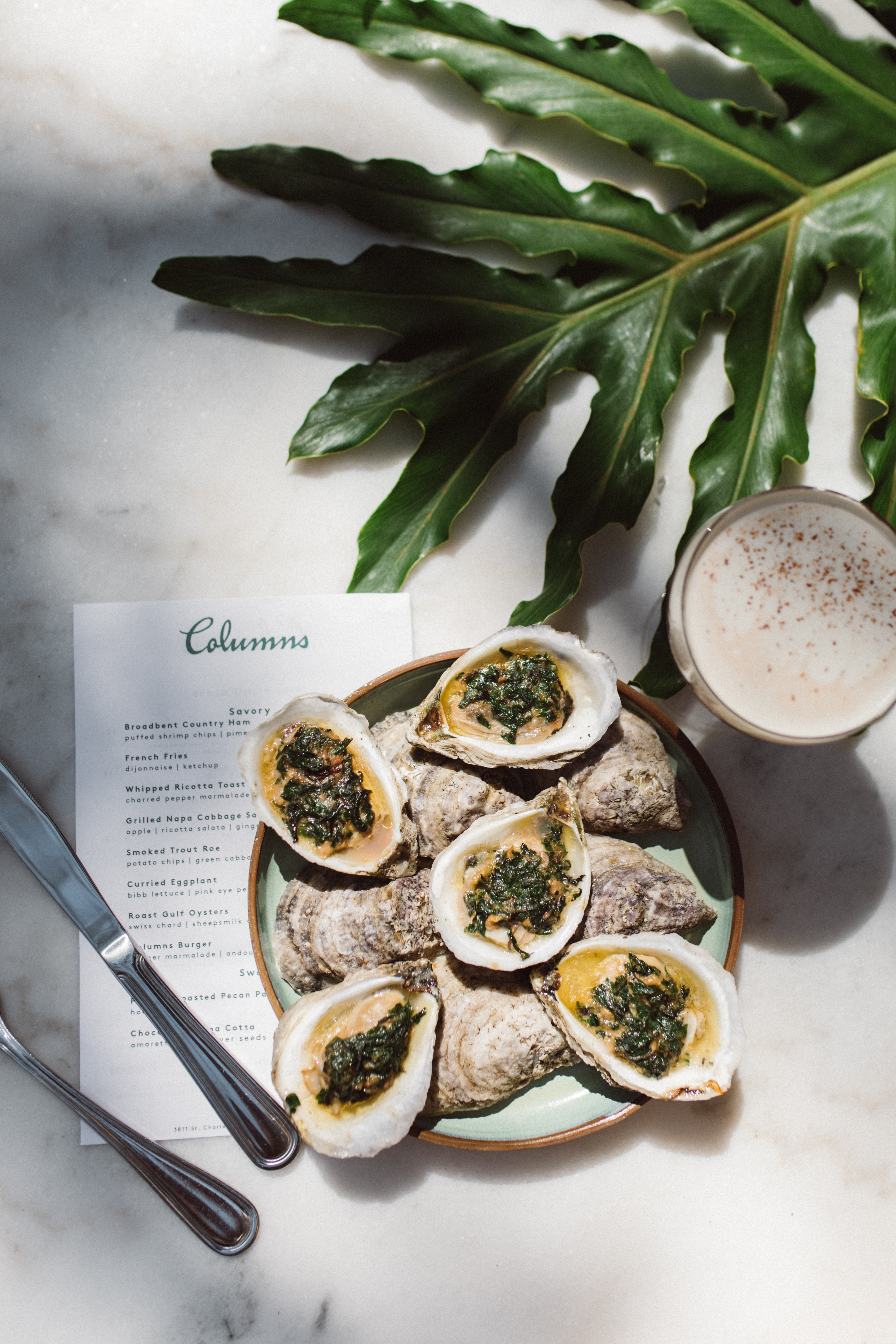 A plate of oysters with a menu and a drink on a marble table.