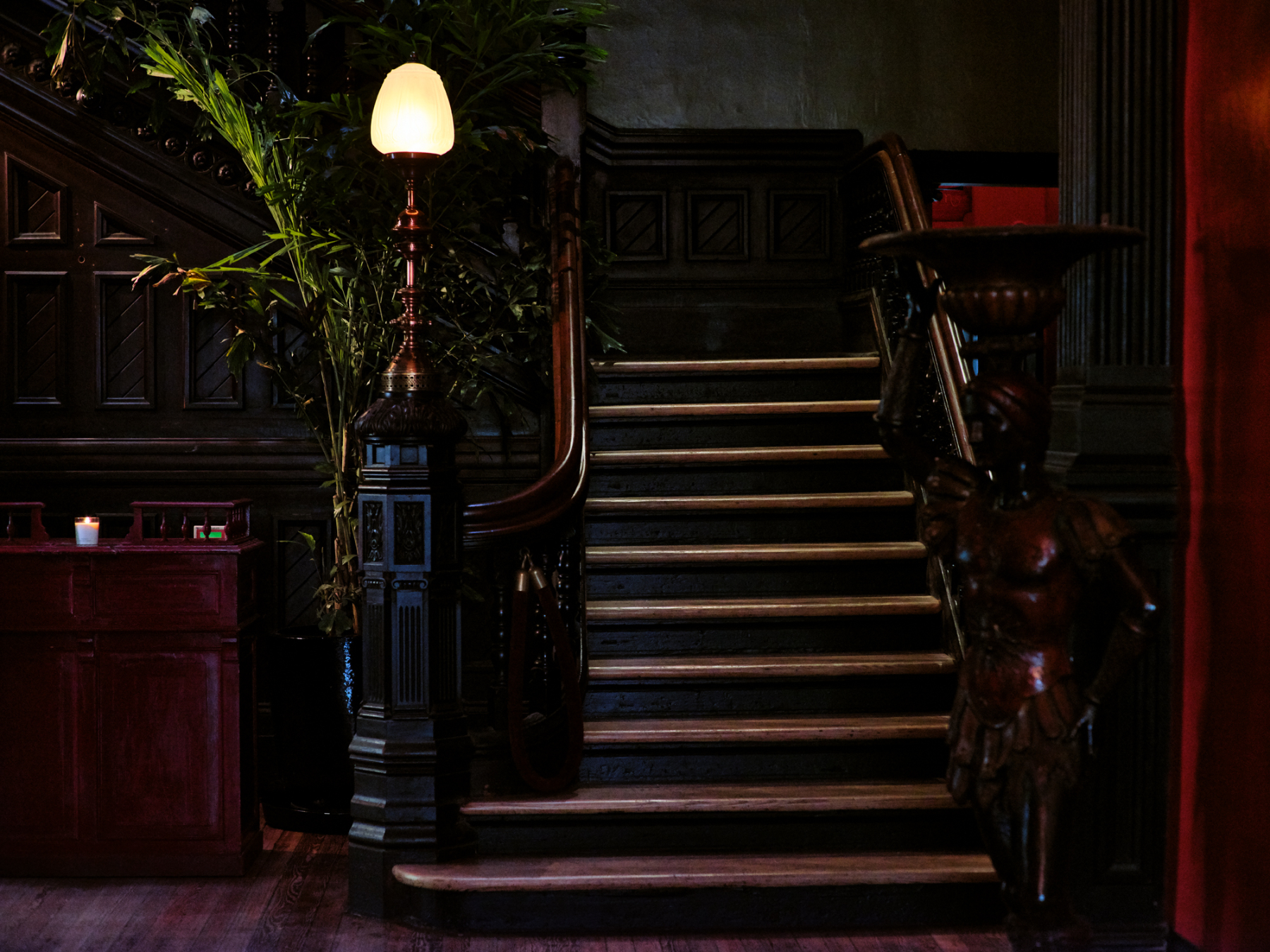 A dimly lit staircase with a wooden railing and a lamp post next to it.