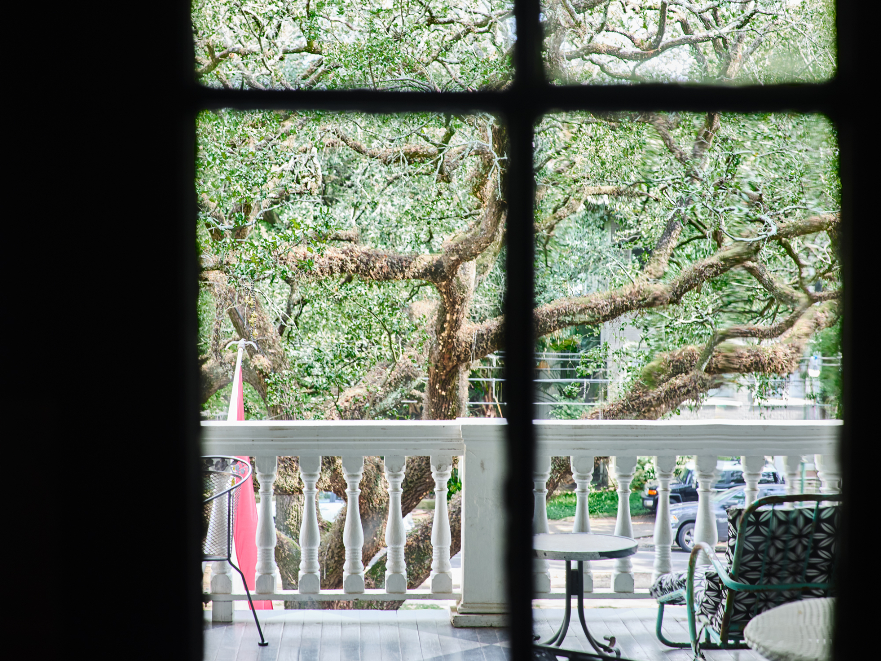 A balcony with a white railing and outdoor furniture overlooking a street with trees.