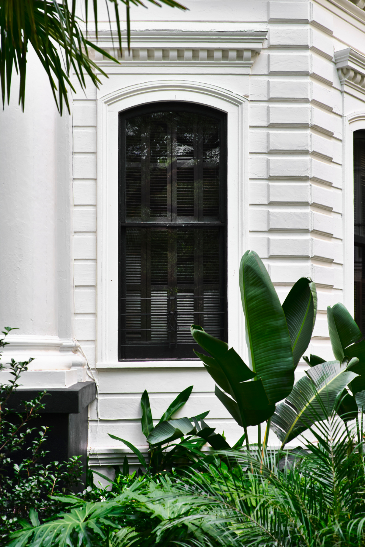 A white building with arched windows and lush greenery in front.