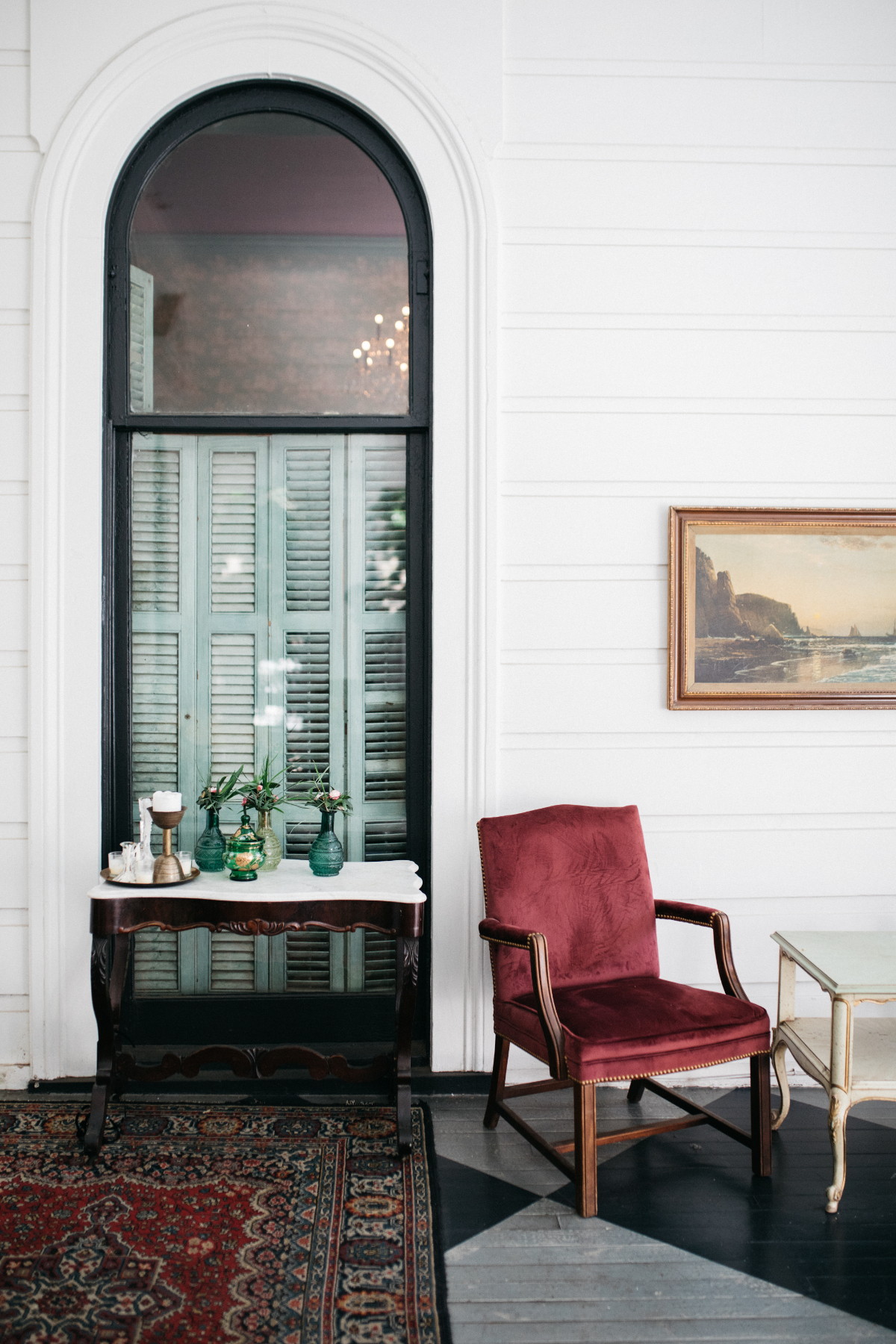 A cozy hotel lobby with a large window, a red chair, and a side table.