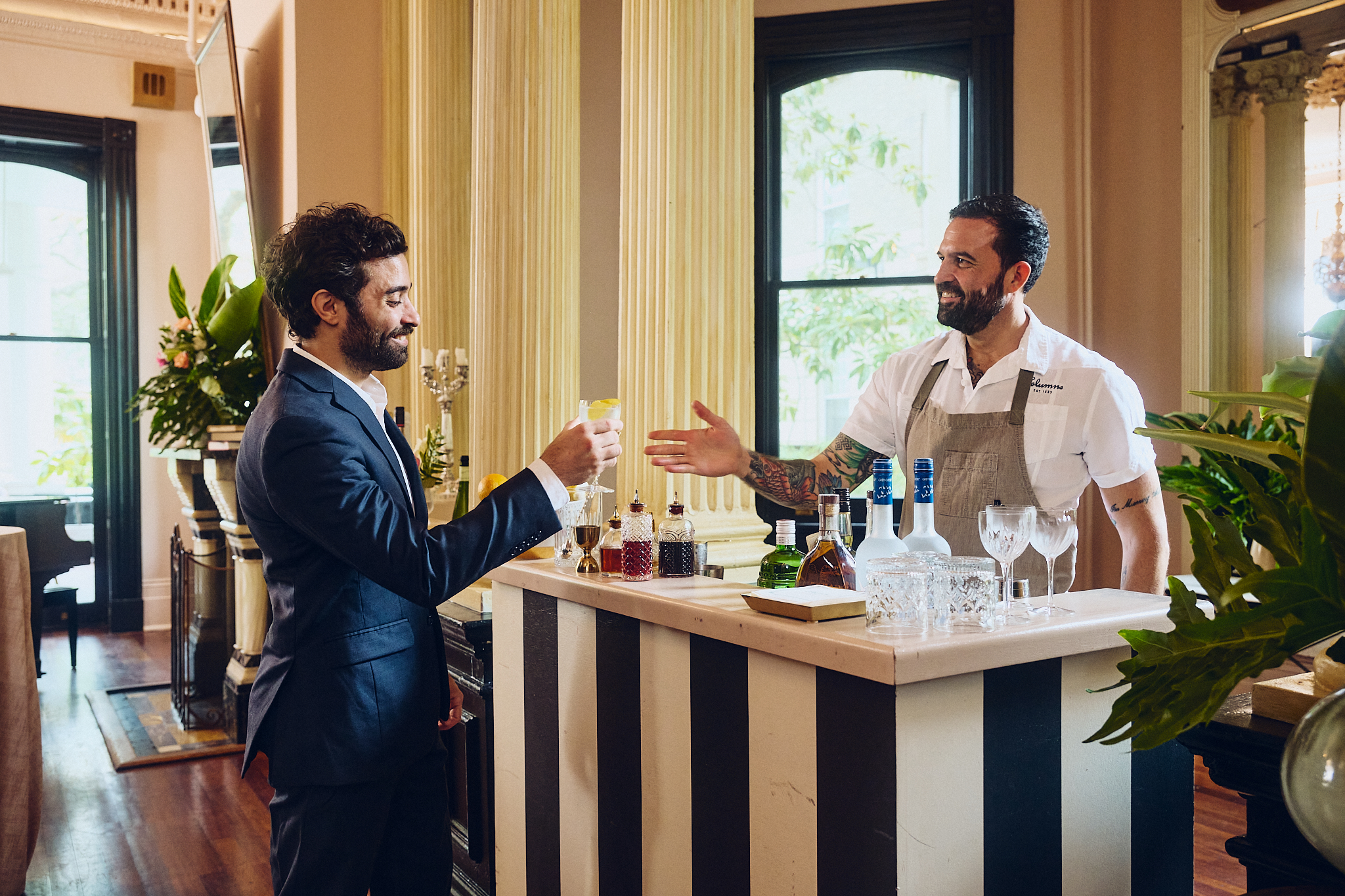 Two men standing at a bar with drinks and bottles