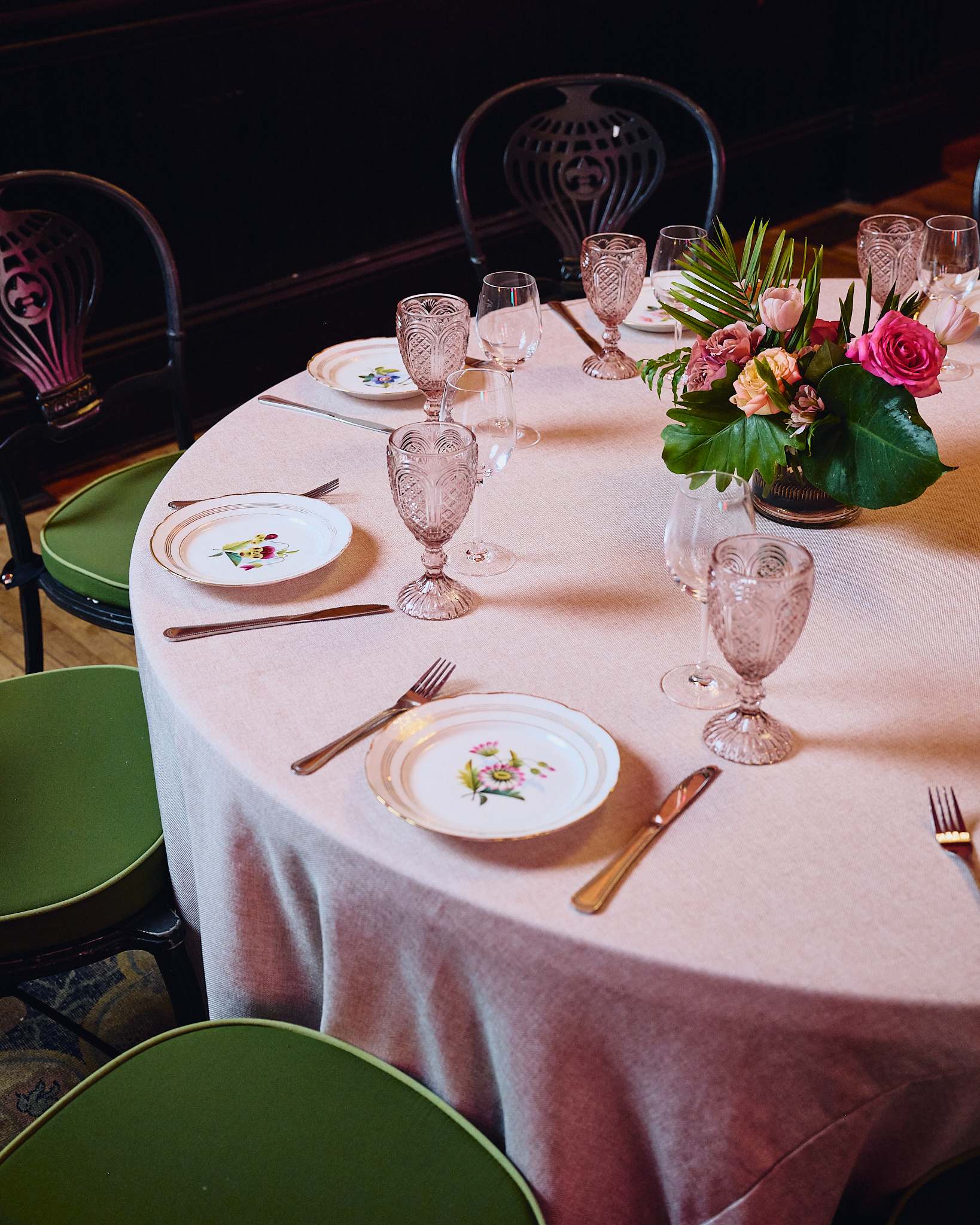 A round dining table set with white plates, pink glasses, and a flower arrangement in the center.