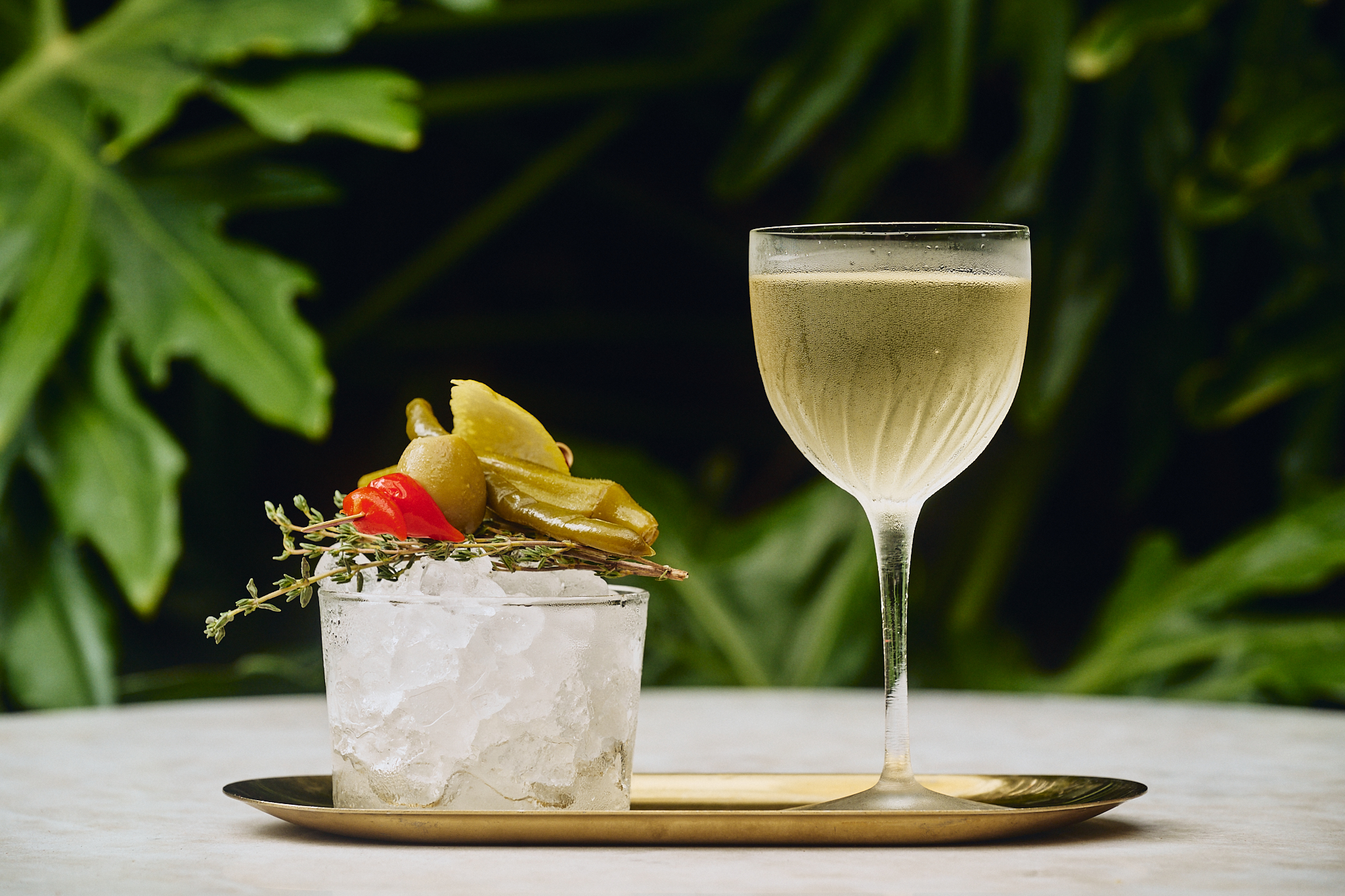 a cocktail with herbs and pickles on a tray
