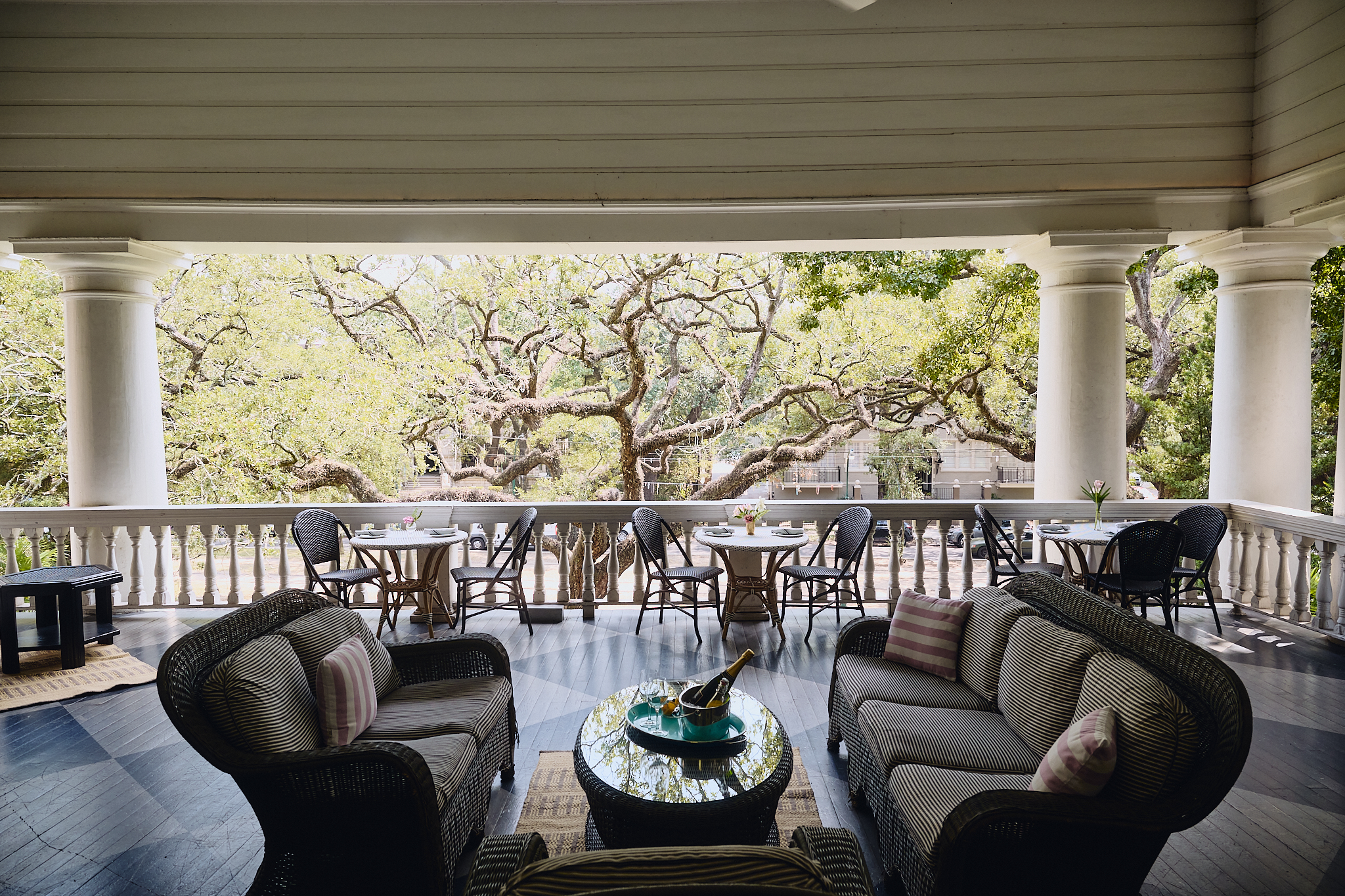 A large porch with columns and outdoor furniture overlooking trees.